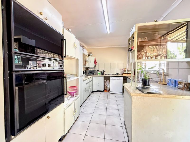 A functional kitchen featuring built-in double ovens, tiled flooring, and ample cabinetry, offering a dated aesthetic ready for modern renovation.