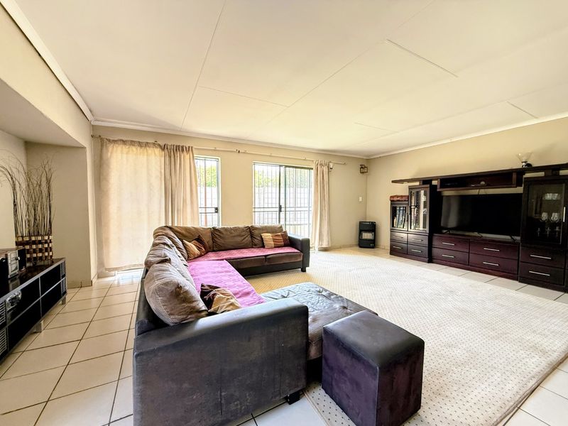 Spacious living room featuring tiled flooring, built-in cabinetry, and sliding glass doors with security gates providing access to the exterior.