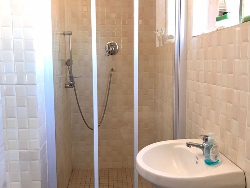 A functional bathroom featuring a shower enclosure with a glass door, a pedestal basin, and neutral wall tiling throughout.