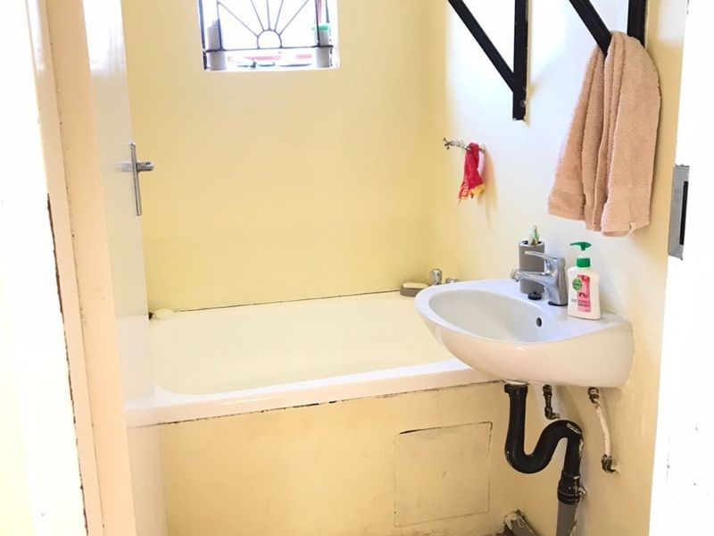 Compact bathroom featuring a bathtub, wall-mounted basin, and security window grille. The space requires cosmetic updates and improved plumbing concealment.