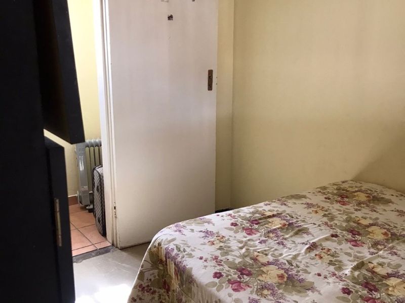 A bedroom featuring tiled flooring and an internal door leading to an adjacent space, showing signs of wear and dated finishes.