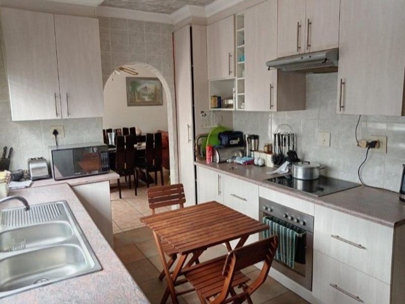 A functional kitchen featuring light-toned cabinetry, laminate countertops, integrated oven and hob, and tiled finishes, with an arched opening leading to the dining area.