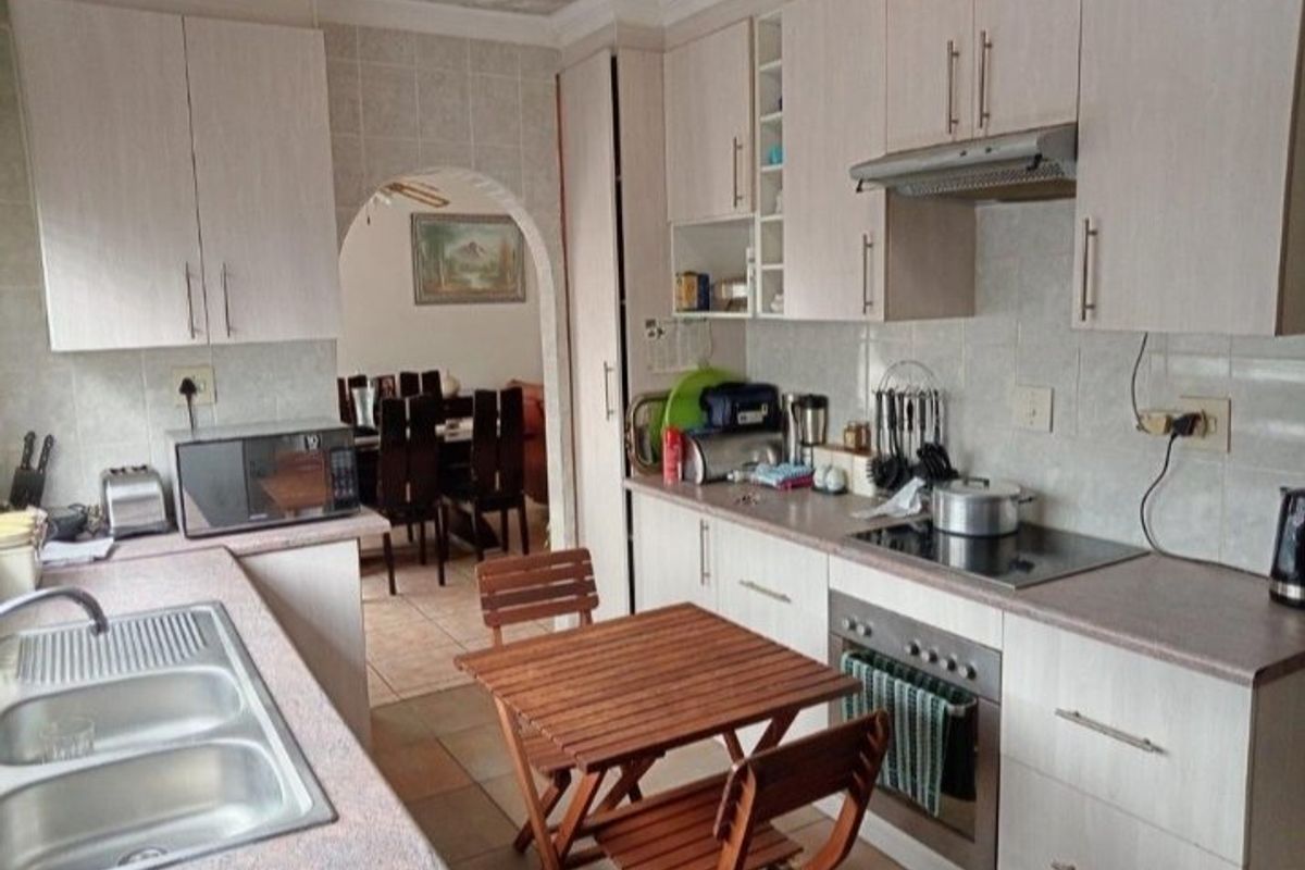 Functional kitchen featuring light-toned cabinetry, laminate countertops, integrated oven and hob, and tiled finishes, with an arched doorway leading to the dining area.
