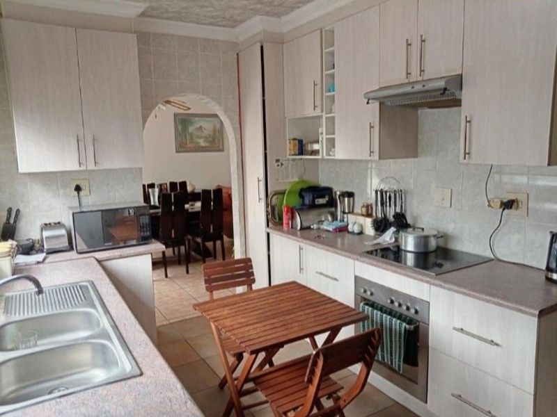 Functional kitchen featuring light-toned cabinetry, laminate countertops, integrated oven and hob, and tiled finishes, with an arched doorway leading to the dining area.