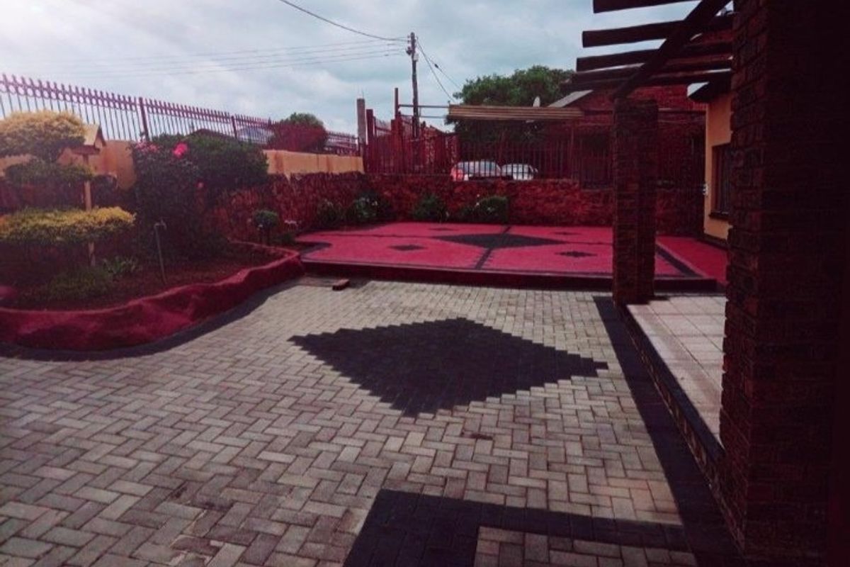 A well-maintained rear courtyard featuring patterned paving, a pergola structure, and raised garden beds enclosed by brick walls and metal fencing.