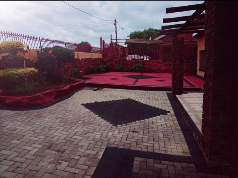 A well-maintained rear courtyard featuring patterned paving, a pergola structure, and raised garden beds enclosed by brick walls and metal fencing.