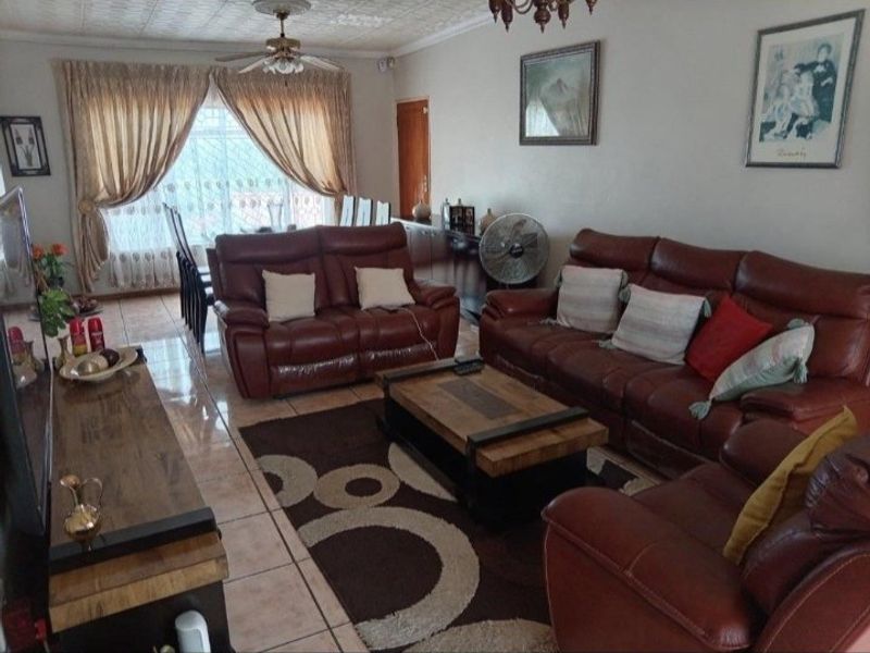 A spacious living room featuring tiled flooring, a ceiling fan, and decorative ceiling tiles, offering a comfortable and functional living space.