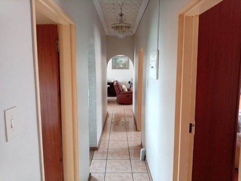 A narrow interior hallway featuring tiled flooring, an arched transition, and a central ceiling light fixture, connecting multiple rooms within the home.
