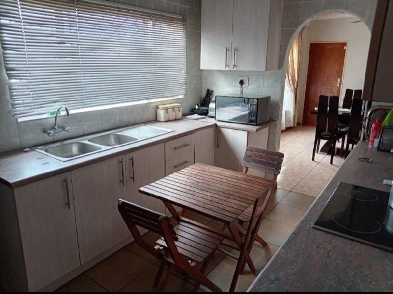 Functional kitchen featuring laminate countertops, double sink, tiled backsplash, and built-in cabinetry, with an open archway leading to the dining area.
