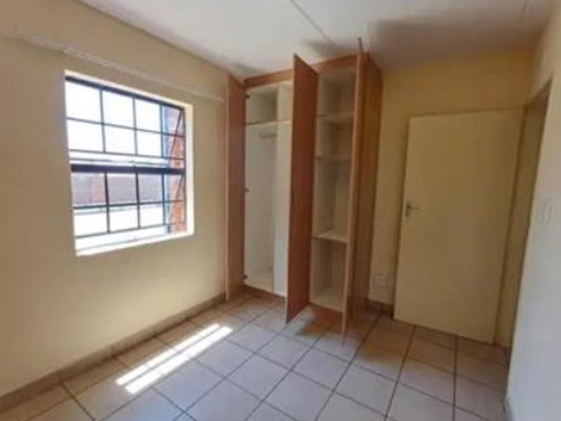 A simple, empty bedroom featuring tiled flooring, a grid-pattern window, and built-in wooden cupboards.