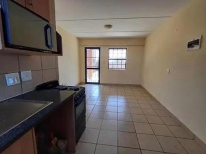 An open-plan kitchen and living area featuring tiled floors, built-in cabinetry, and access to an exterior door with a security gate.