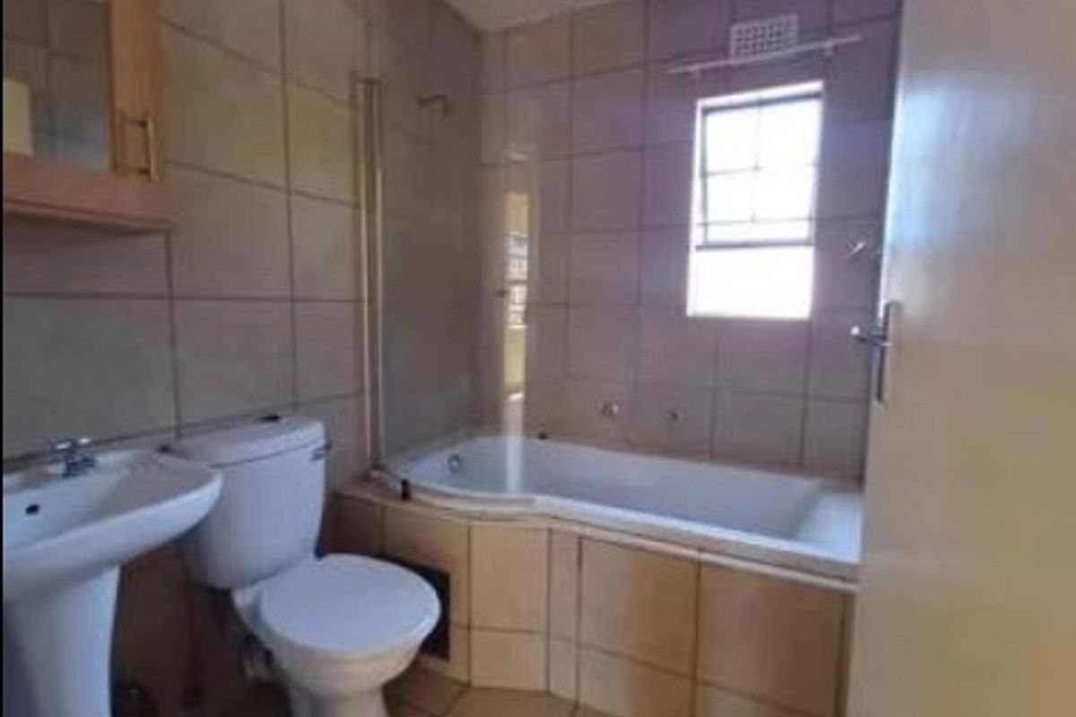 A functional bathroom featuring a pedestal basin, toilet, and a built-in bathtub with a glass shower screen, finished with neutral wall and floor tiles.