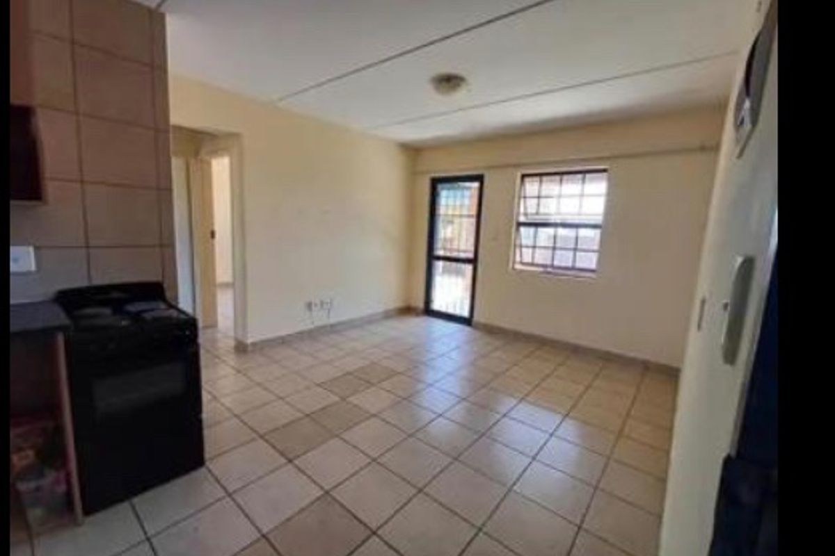 An open-plan living and kitchen area featuring tiled flooring, a built-in stove, and access to an outdoor space through a security gate.