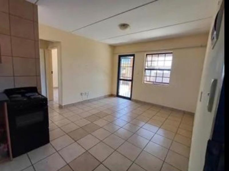 An open-plan living and kitchen area featuring tiled flooring, a built-in stove, and access to an outdoor space through a security gate.