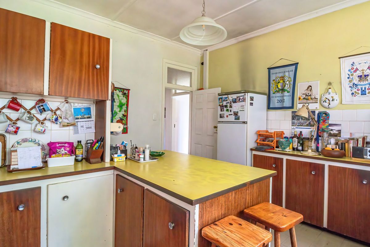 A dated kitchen featuring original wood-tone cabinetry, laminate countertops, and a tiled backsplash, offering significant potential for a modern renovation.