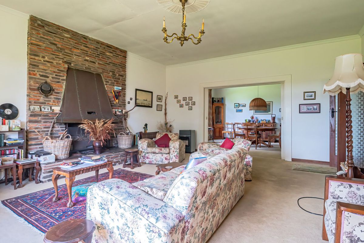 Spacious living room featuring a prominent brick fireplace with a metal hood, decorative ceiling rose, and coving, leading into an adjacent dining area.