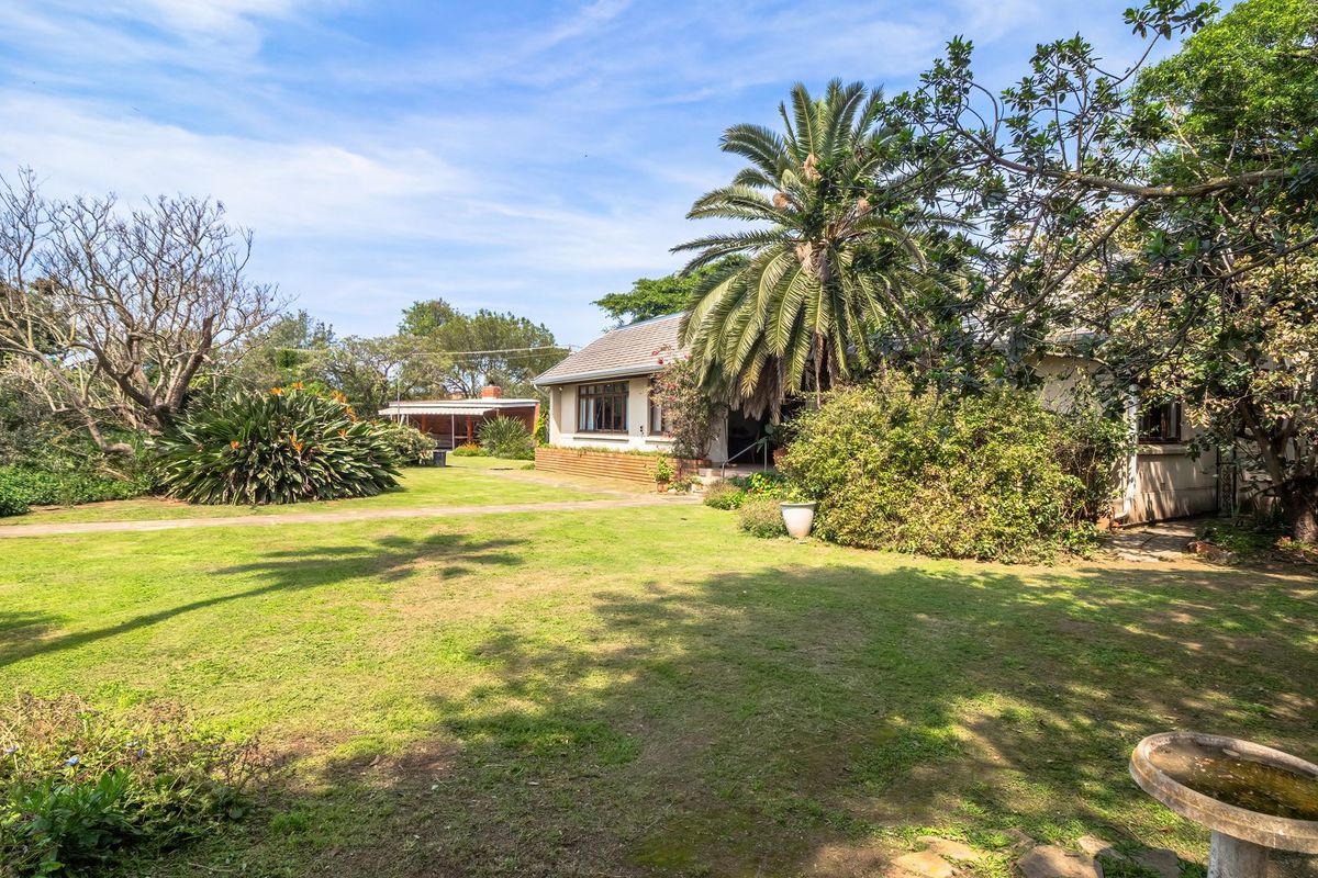 A spacious rear garden featuring a well-maintained lawn, mature trees, and a view of the rear building elevation.
