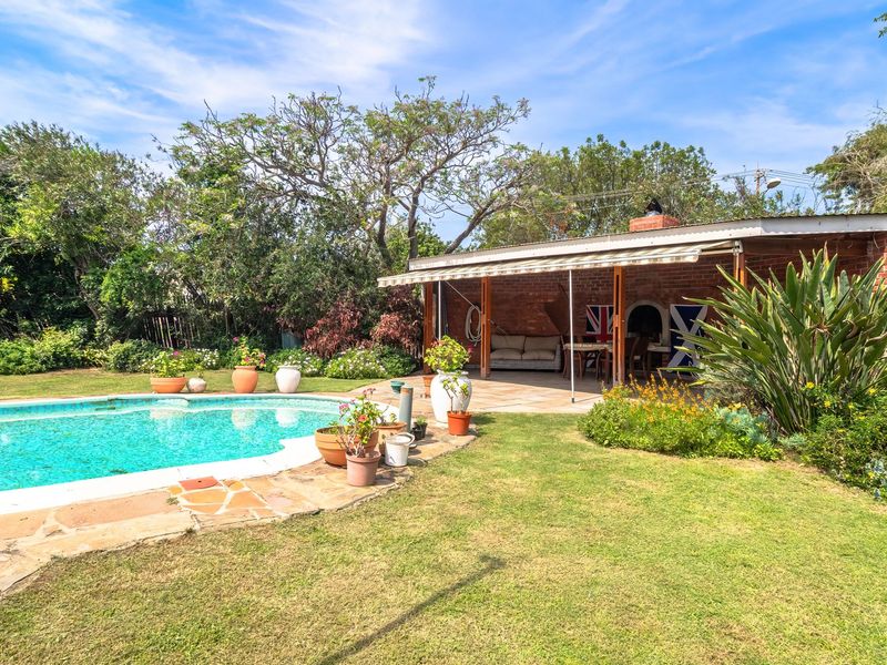 Outdoor entertainment area featuring a swimming pool, stone patio, and a covered brick braai area set within a landscaped garden.