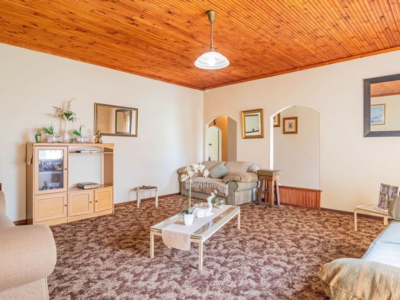 Spacious living room featuring a warm timber tongue and groove ceiling, neutral walls, and classic archway transitions to adjacent areas.