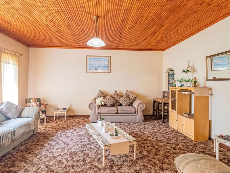 A spacious living room featuring a distinctive timber tongue and groove ceiling and patterned carpet flooring, offering a traditional aesthetic with potential for modernization.
