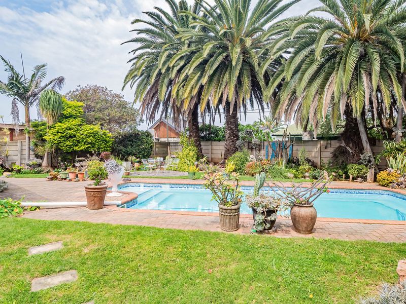 A backyard pool area featuring a swimming pool, brick paved surround, and established palm trees within a private garden setting.