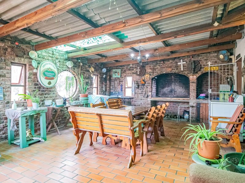 Spacious covered patio featuring exposed brick walls, timber beam ceiling, and a large built-in braai, perfect for outdoor entertaining.