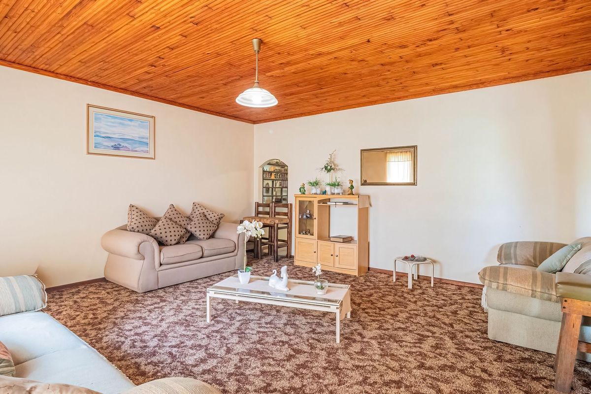 Spacious living room featuring a traditional timber tongue and groove ceiling and carpeted flooring, offering a classic layout ready for modern updates.