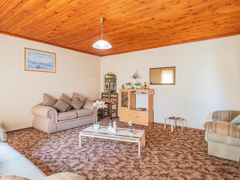Spacious living room featuring a traditional timber tongue and groove ceiling and carpeted flooring, offering a classic layout ready for modern updates.