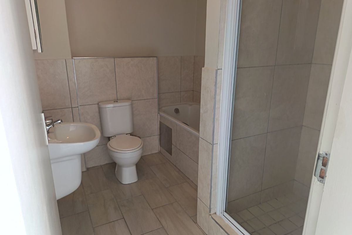 A clean, functional bathroom featuring a pedestal basin, toilet, bathtub, and a separate shower enclosure with neutral wall and floor tiling.