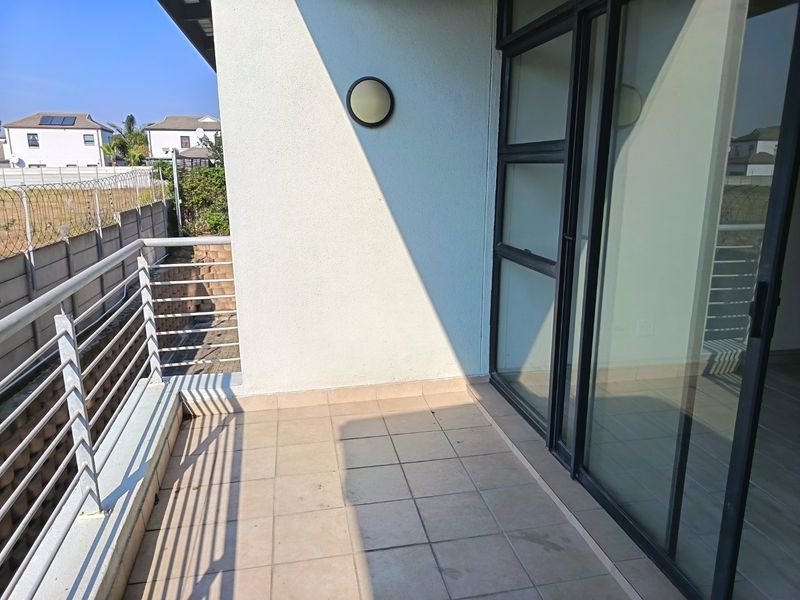 A clean, tiled balcony featuring a metal balustrade and large sliding glass doors, providing a functional outdoor space with a view of the surrounding area.