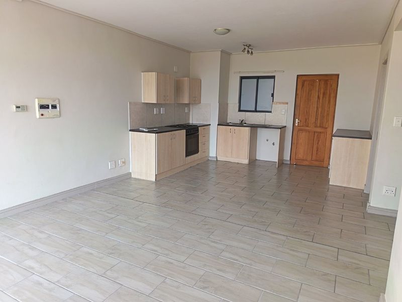 An open-plan kitchen and living area featuring light wood cabinetry, tiled flooring, and a built-in oven, offering a clean and functional space.