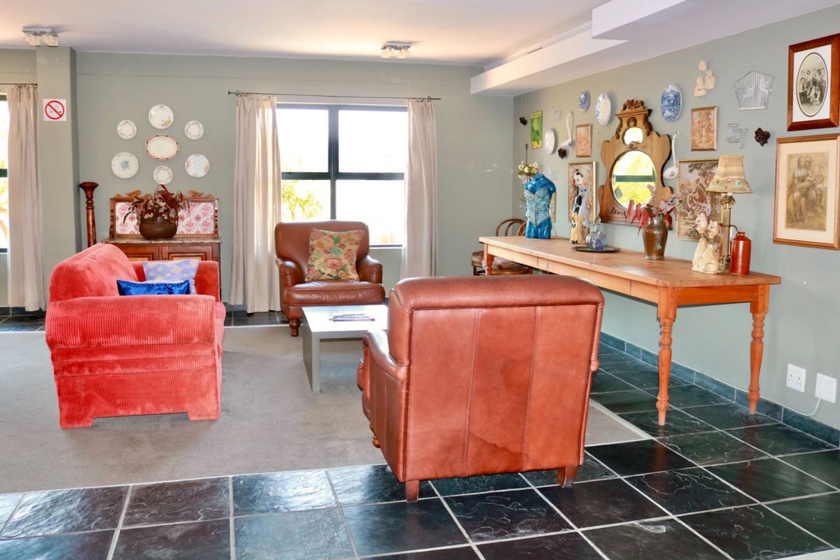 A spacious living room featuring a combination of dark tiled flooring and carpet, neutral wall tones, and natural light from a large window.