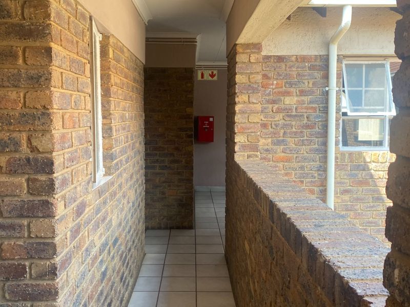 An exterior apartment hallway featuring face brick walls, tiled flooring, and a wall-mounted fire extinguisher.