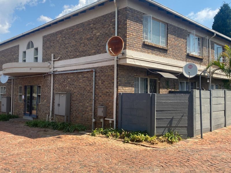 Exterior view of a face brick apartment complex featuring a paved driveway, precast boundary walls, and multiple satellite dish installations.