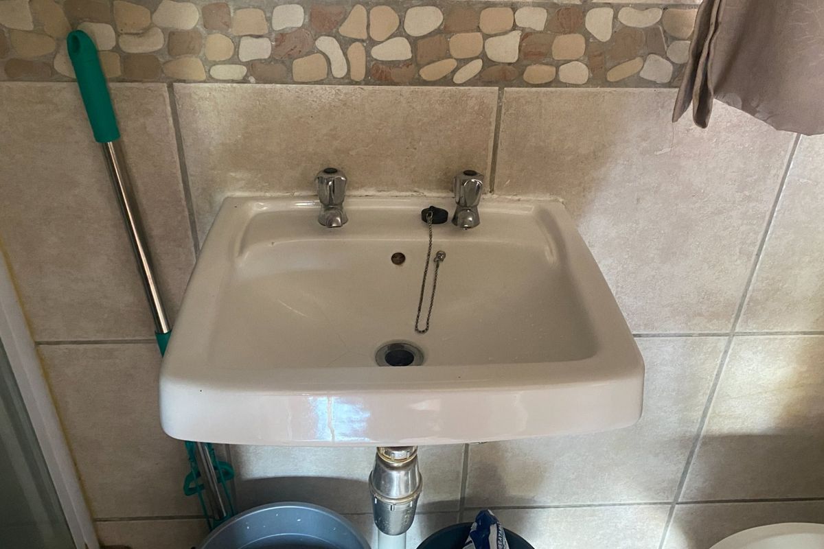 A functional bathroom basin featuring chrome pillar taps and decorative stone-effect wall tiling, presenting a dated but serviceable aesthetic.