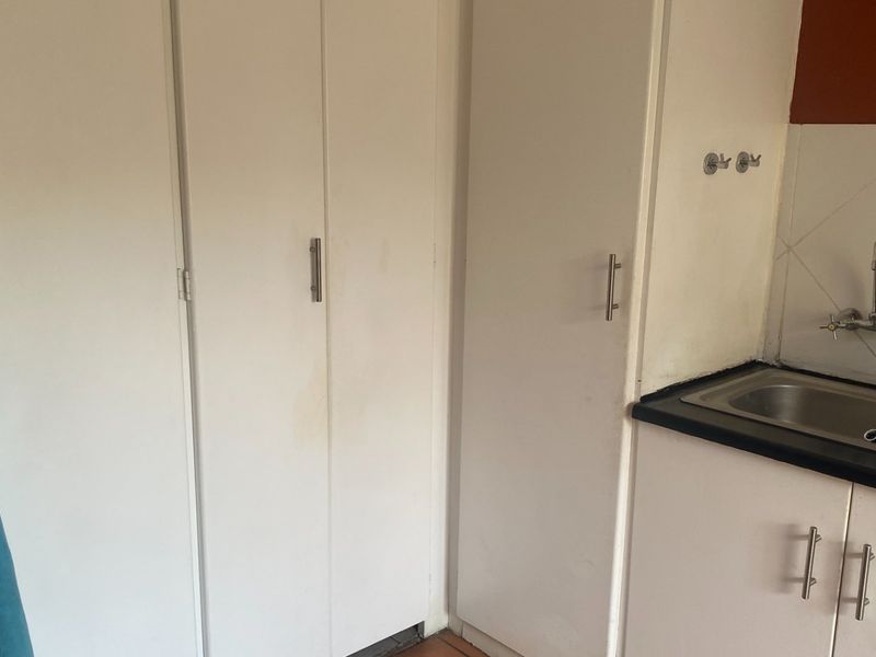 A functional laundry area featuring built-in white cabinetry, a stainless steel sink, and a tiled backsplash.