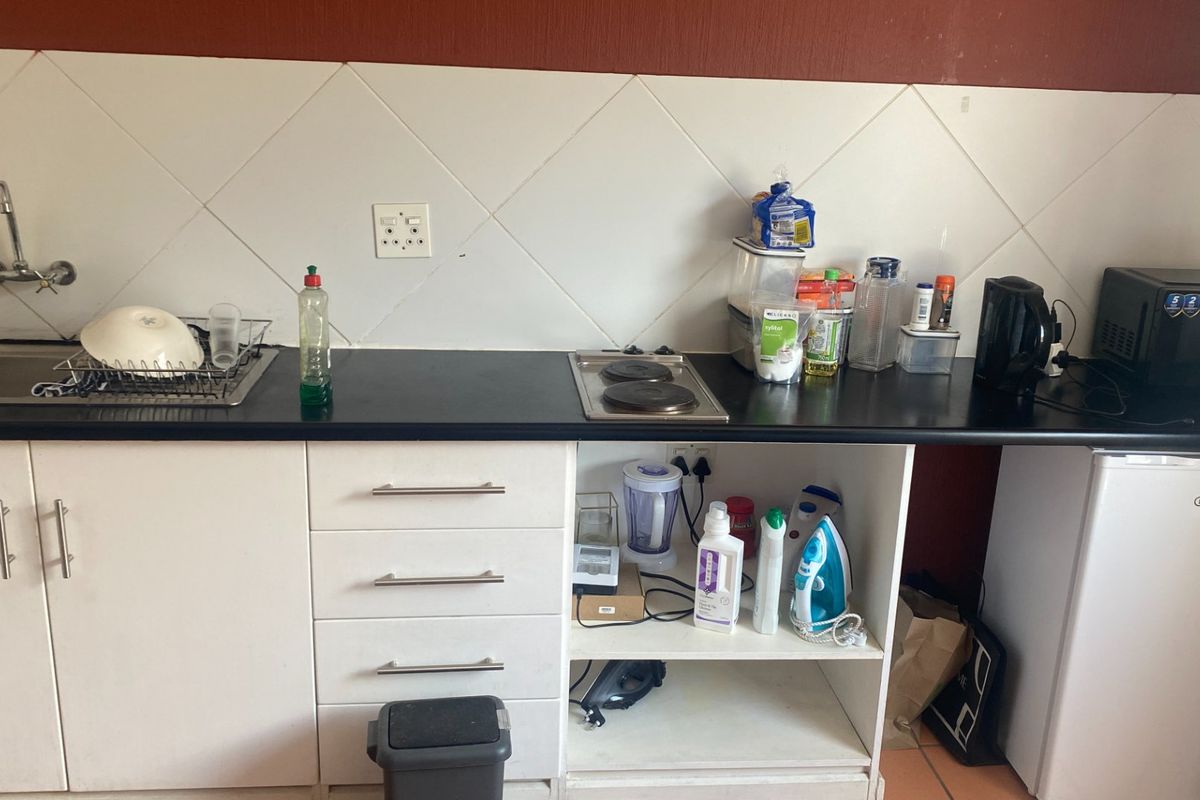 A compact kitchen area featuring white cabinetry, a dark laminate countertop, a stainless steel sink, and a built-in electric hob with tiled backsplash.