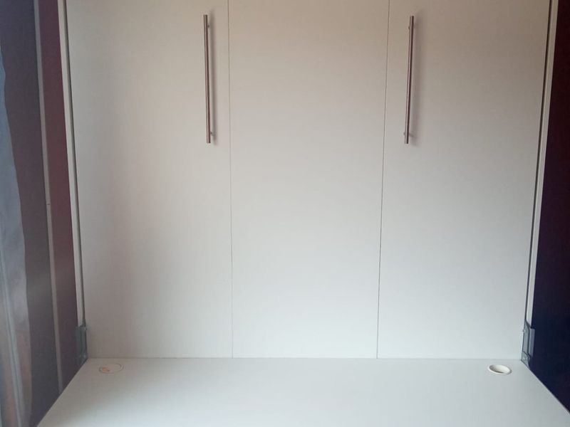 A functional bedroom space featuring a white built-in murphy bed with an integrated desk unit and convenient electrical power points.