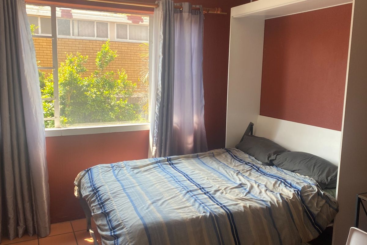 A bedroom featuring a built-in wall bed unit and tiled flooring, with natural light provided by a large window.