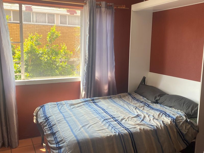 A bedroom featuring a built-in wall bed unit and tiled flooring, with natural light provided by a large window.