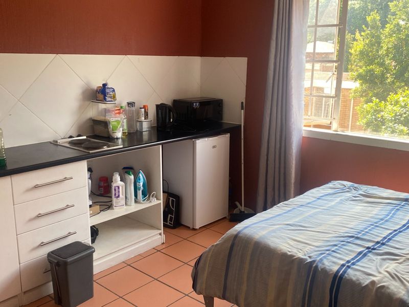 Compact open-plan studio apartment featuring a kitchenette with built-in cabinetry, electric hob, tiled backsplash, and ceramic floor tiles.
