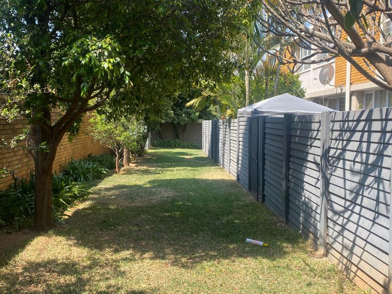 A private side garden area featuring a well-maintained lawn, mature trees, and a combination of brick and timber slat boundary fencing.