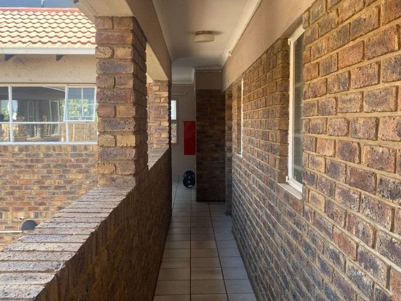 A covered exterior walkway or balcony featuring face brick walls and tiled flooring, providing access to the apartment units.