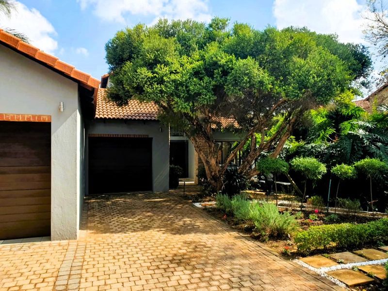 Front exterior view of the house featuring a paved driveway, garage, and a well-maintained landscaped garden with a large mature tree.