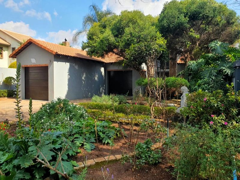 Front view of the property featuring a tiled roof, garage, paved driveway, and a well-established landscaped garden.