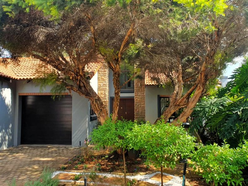 Front elevation of a house featuring stone cladding, a tiled roof, a double garage, and a landscaped garden with mature trees.