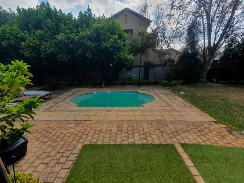 Outdoor pool area featuring a paved surround, artificial grass sections, and established garden landscaping with a perimeter wall.