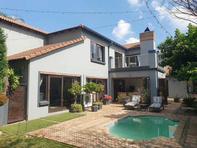 Rear view of the house featuring a swimming pool, paved patio area, upper-level balcony, and well-maintained exterior finishes.