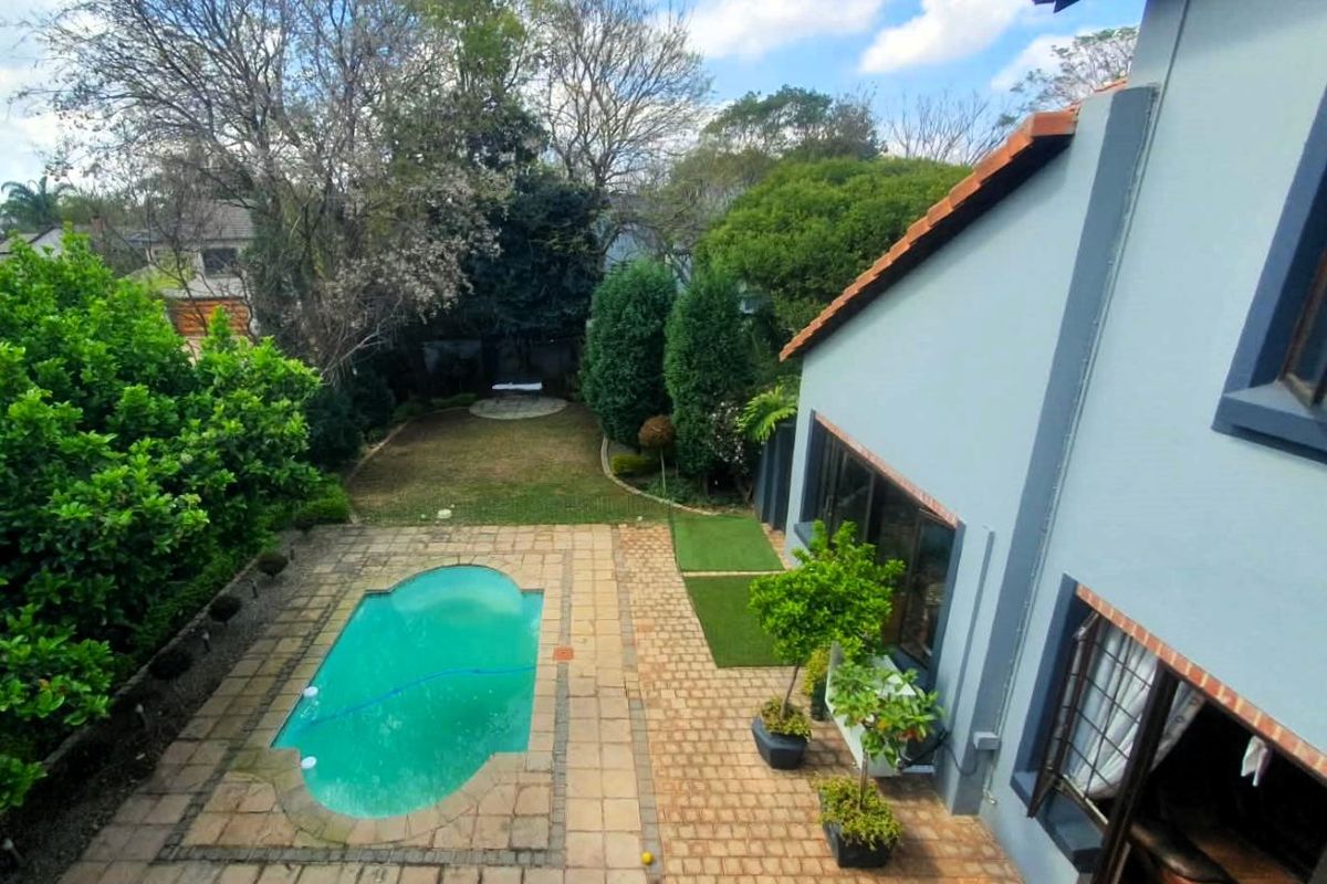 Elevated view of a rear garden featuring a swimming pool, paved patio area, and established landscaping adjacent to the main house structure.
