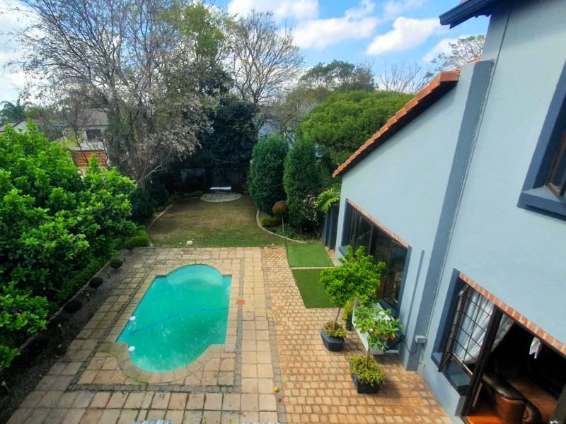 Elevated view of a rear garden featuring a swimming pool, paved patio area, and established landscaping adjacent to the main house structure.